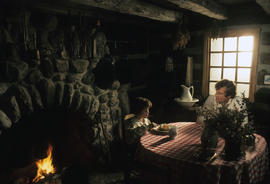 Actors at table in front of fireplace
